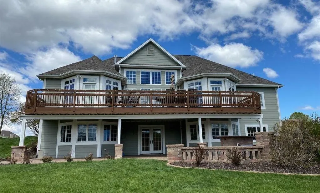 Two-story gray house with wooden deck balcony and stone accents under blue sky
