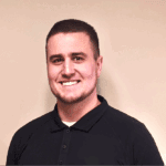 Professional headshot of smiling young man in black polo shirt against beige background