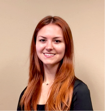 Professional headshot of smiling young woman with long red hair wearing black blazer