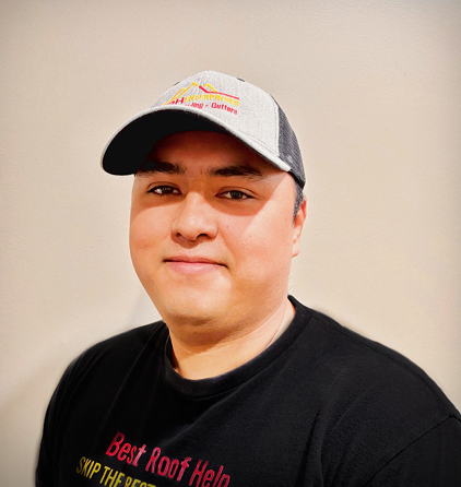 Man wearing a cap and black t-shirt in a neutral setting.
