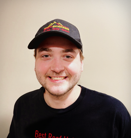 Smiling man wearing a branded black cap and t-shirt indoors.
