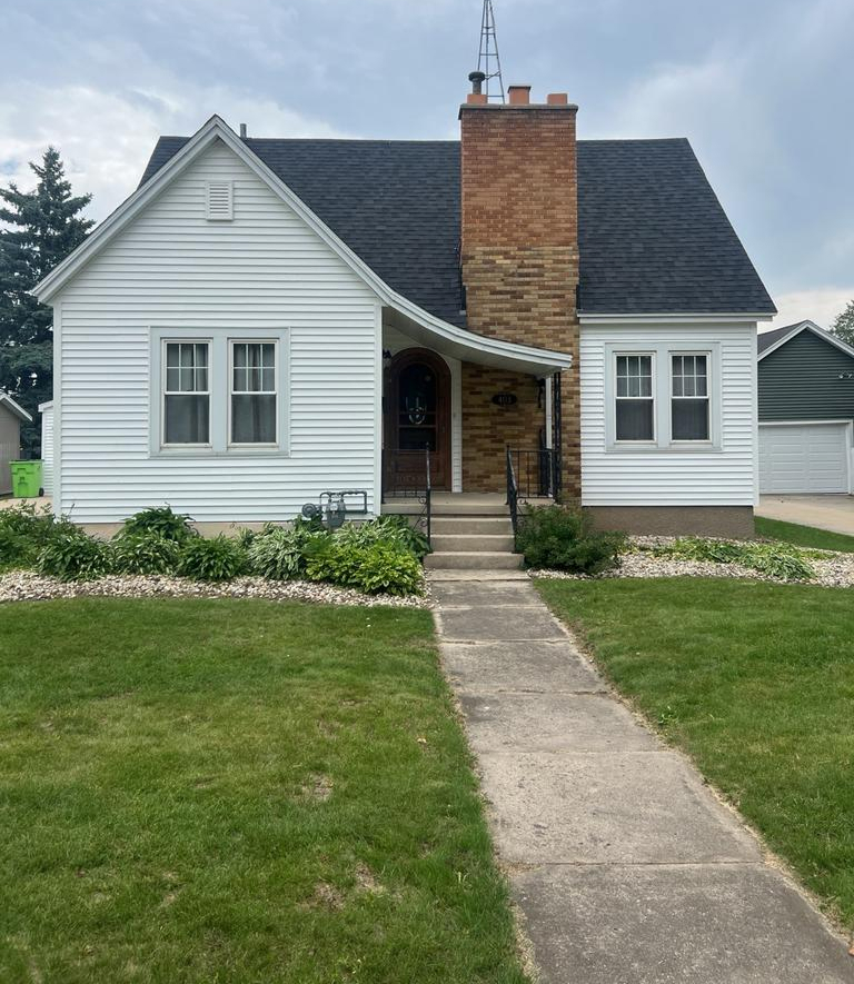 Charming small white house with brick chimney and front lawn.